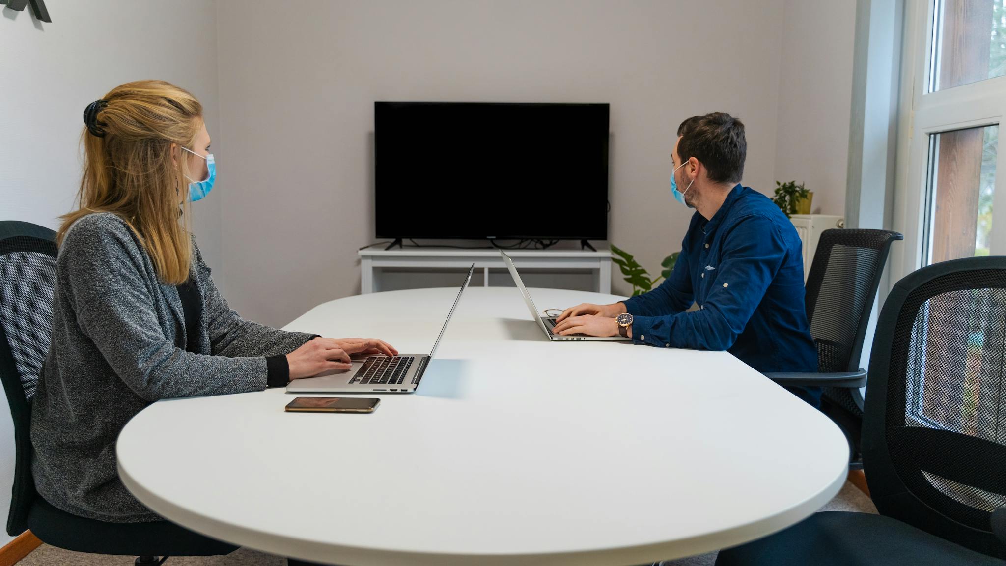 Two employees wearing face masks working on laptops in a modern office workspace.