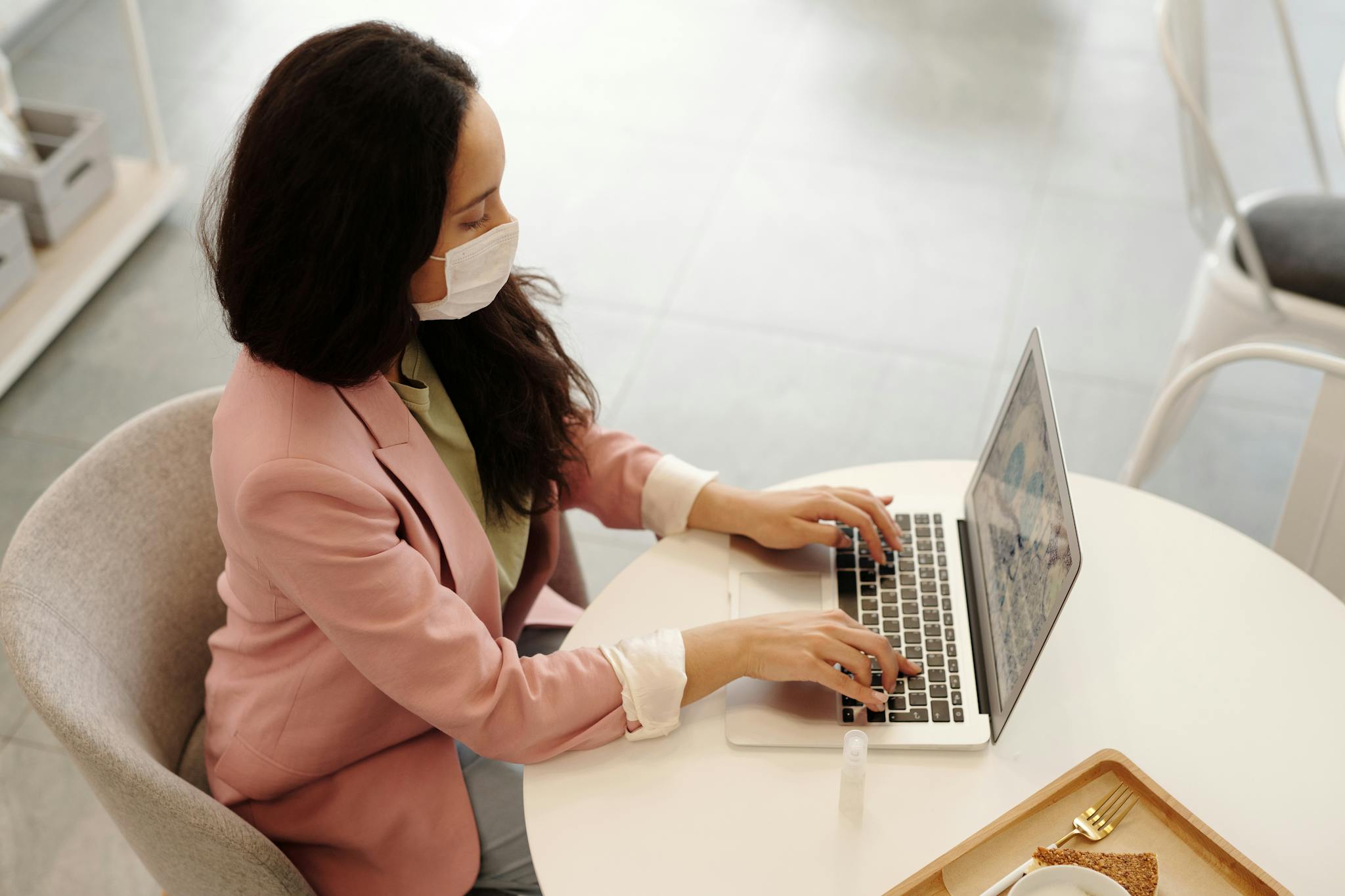 Woman wearing a face mask working on a laptop in a modern indoor setting, embodying new normal work habits.